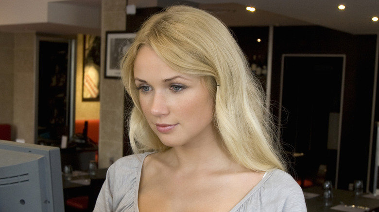 A hostess standing at a computer terminal in a restaurant