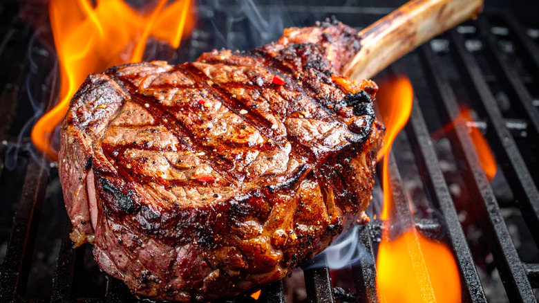 A tomahawk steak being cooked on a grill over flames