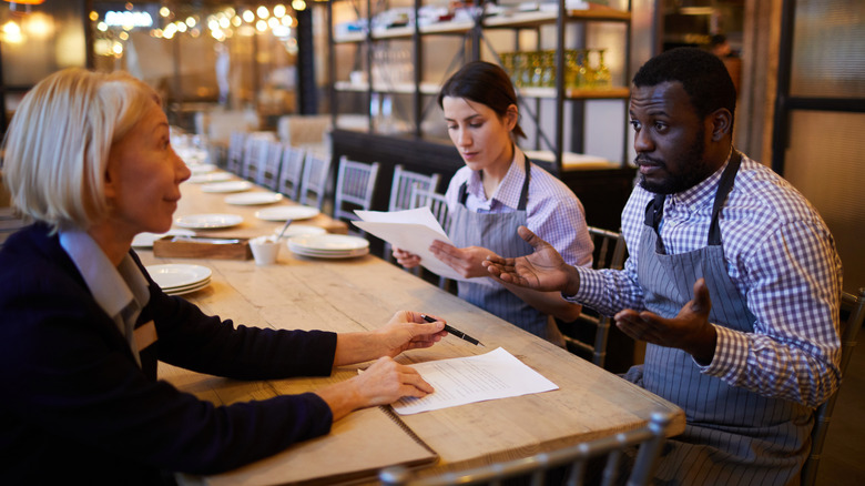 A restaurant manager sitting at a table with two servers
