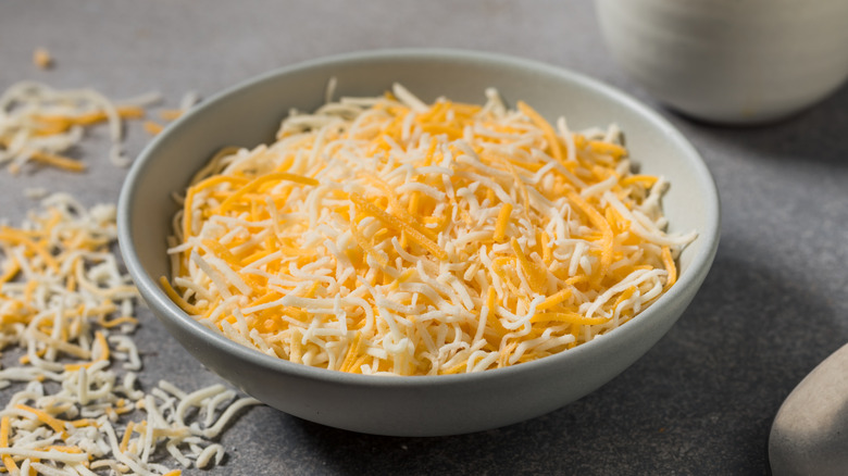 Bowl of shreeded cheese with loose cheese beside it