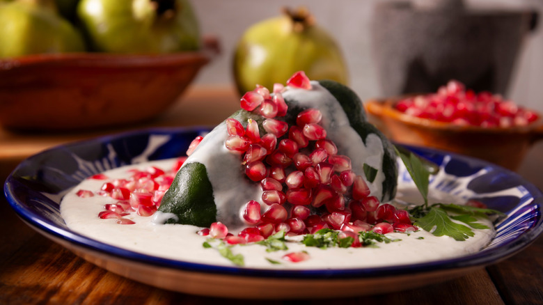 Chiles en nogada served on blue ceramic plate with persimmons in backdrop