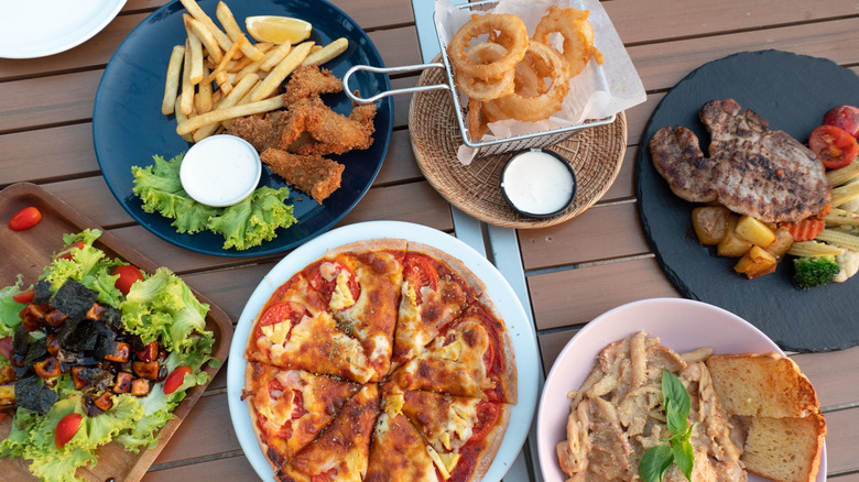 Pizza, steak, burger, and onion rings on wooden table