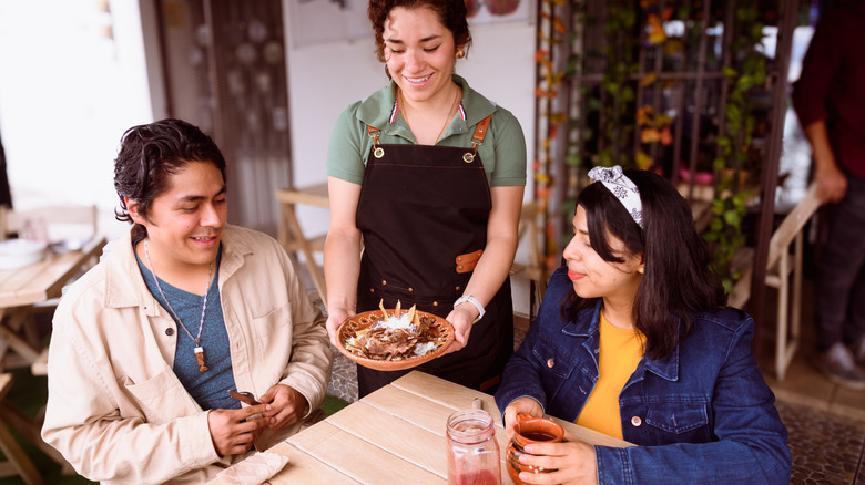 Server presents a dish to two diners at a Mexican restaurant