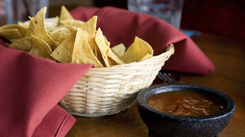 Basket with tortilla chips wrapped in red napkin by salsa ramekin