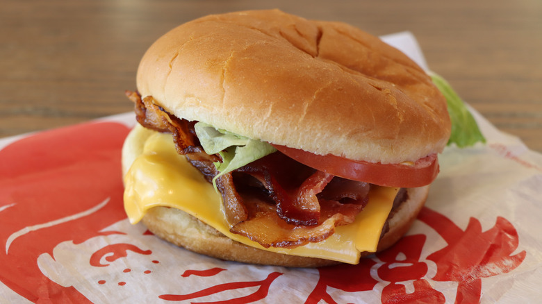 Hamburger with bacon, cheese, lettuce, and tomato on white with Wendy's red pigtailed girl logo