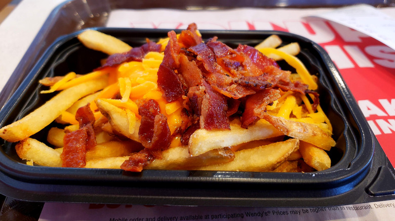 Wendy's fries with cheese and bacon in a square black plastic container on a tray with white and red paper