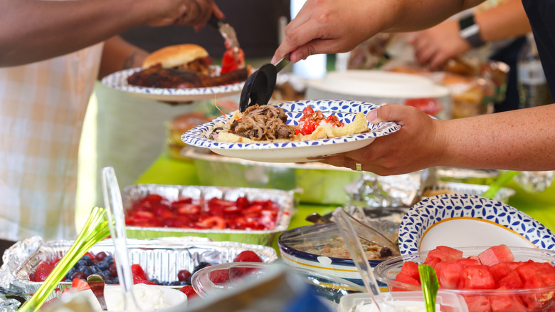 Hands put food on paper plate over potluck spread