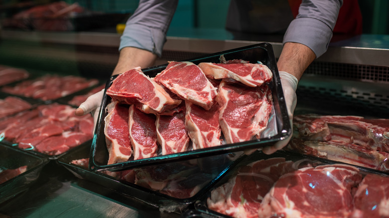 A butcher holding up a black tray with steaks on it.