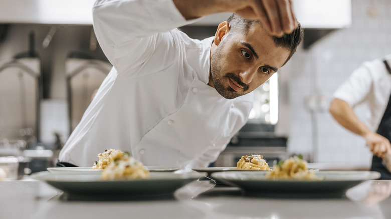 A chef plates pasta dishes in a restaurant kitchen