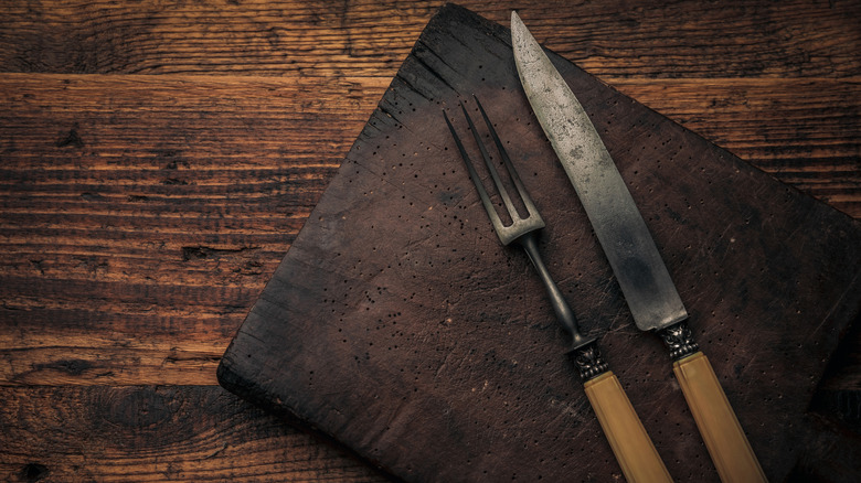 A knife and a fork with a large amount of patina on a darkened board