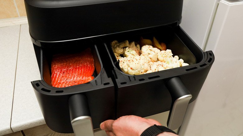 Hand pulling open double basket air fryer with salmon and cauliflower