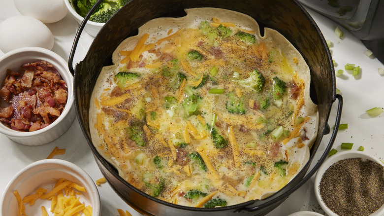An air fryer open tortilla wrap with grated cheese, broccoli, and bacon