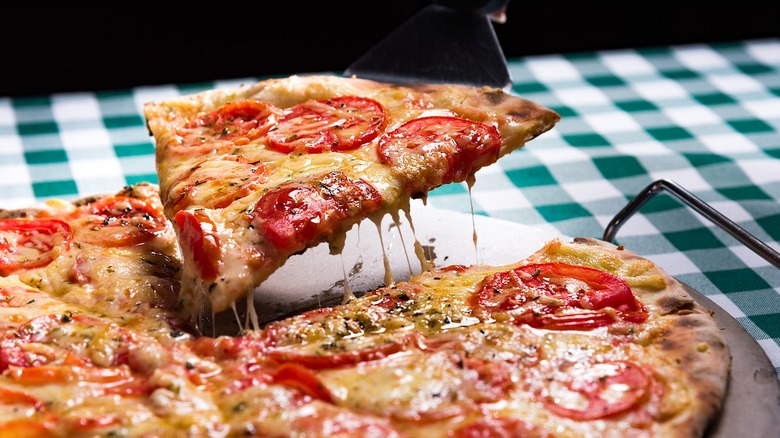 Slice of pepperoni pizza being lifted with spatula with checkered tablecloth underneath