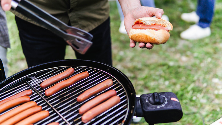 A person cooking hot dogs on a charcoal grill