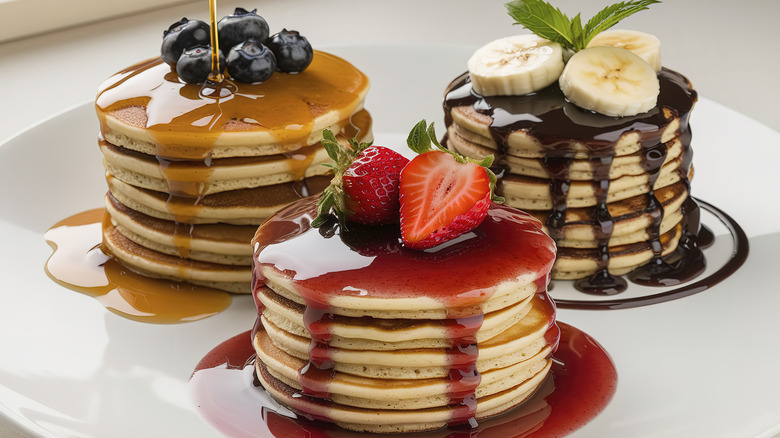 Three stacks of small pancakes on a white plate with different colored syrups and fruits on top