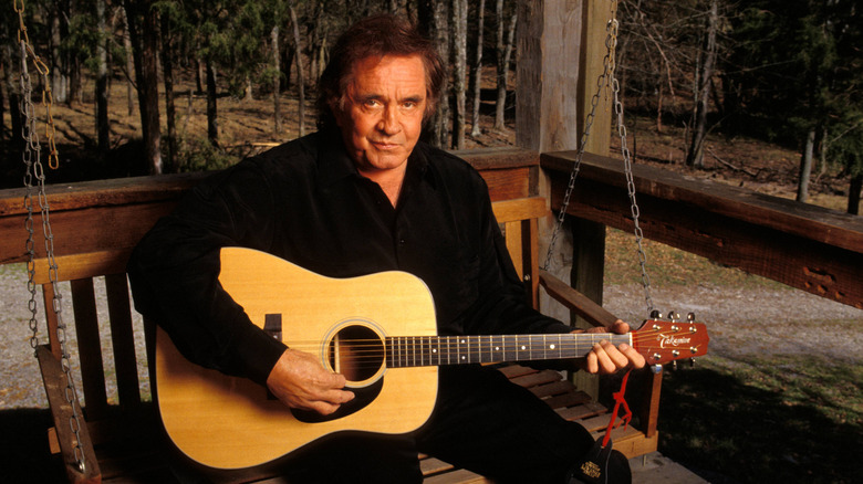 Johnny Cash sits on a porch swing, holding a guitar