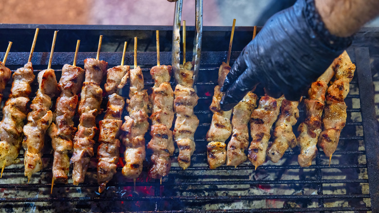 A man is turning over chicken skewers lined up over a hot charcoal grill.
