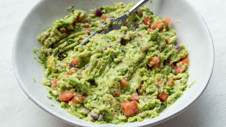 mashed avocado with tomato and onion in a white bowl