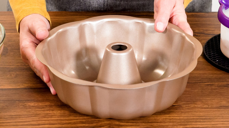 Hands holding a metal Bundt pan on a wooden counter
