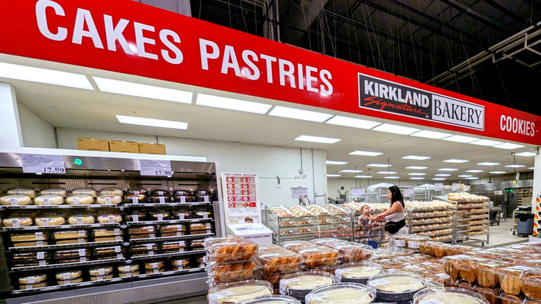 Costco bakery with shelves full of various pies and cakes and a shopper in the background.