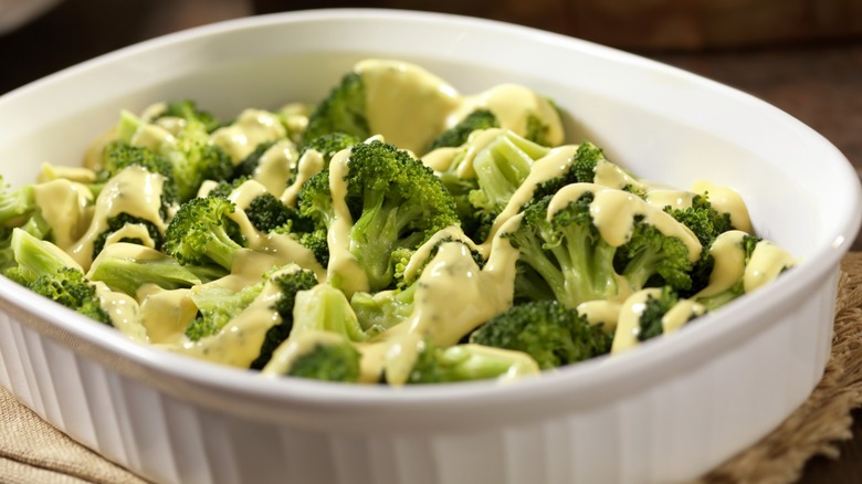 Broccoli topped with cheese sauce in white serving dish