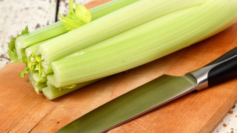 celery stalks and a kitchen knife on a wooden board