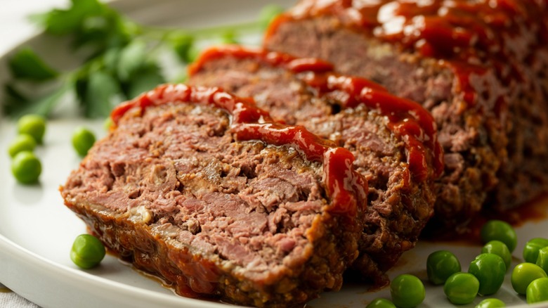 Slices of meatloaf, topped with ketchup and garnished with green peas
