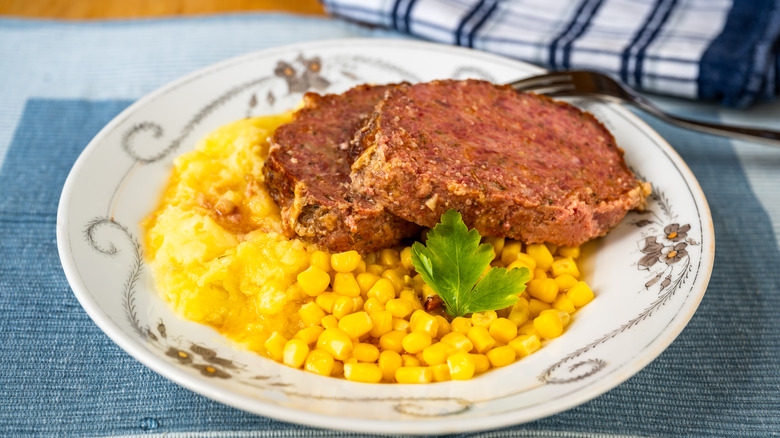 Two slices of meatloaf with corn and mashed potatoes on a white plate