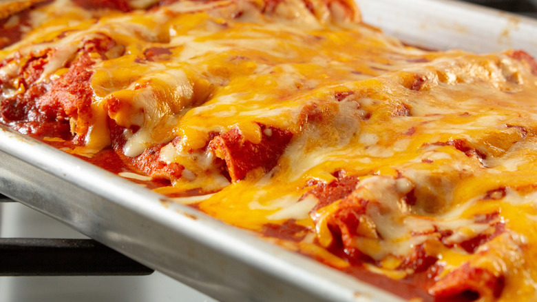 Ceramic casserole tray filled with enchiladas and cheese.