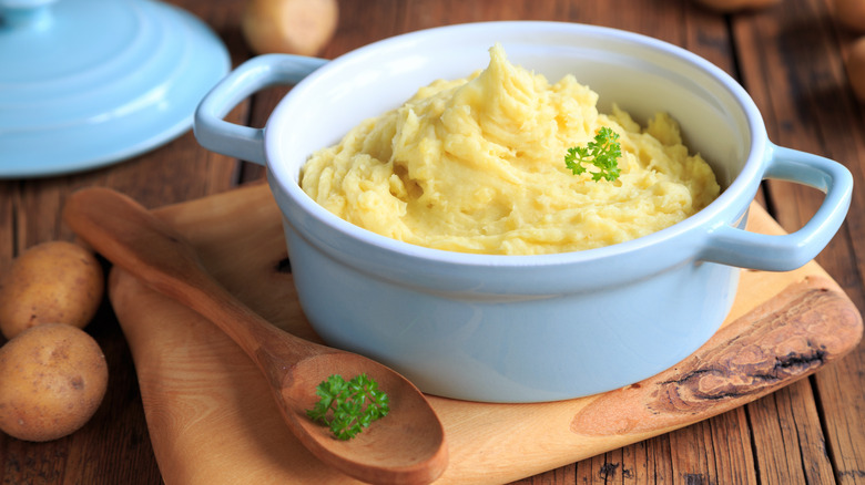 mashed potatoes in ceramic dish with spoon and fresh parsley