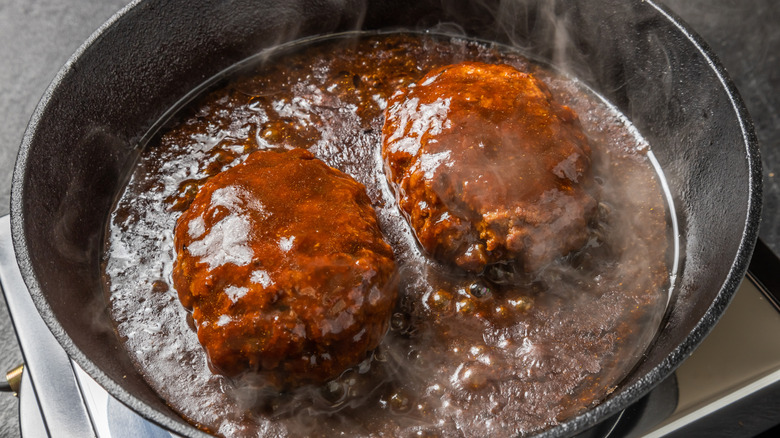 Hamburger patties cooked in sauce in a cast iron skillet.