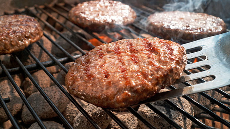 Close-up of burger patty getting flipped with a spatula on barbecue grill.