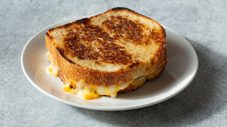 Gooey cheese seeping out of a sourdough grilled cheese sandwich on a white plate.