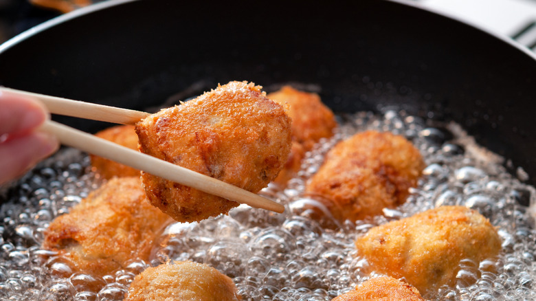 A pair of chopsticks pinches a croquette over hot oil