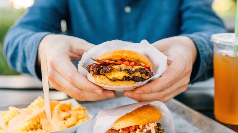 A fast food hamburger being held up to the camera.
