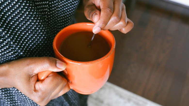 A person stirs an orange mug of coffee with a spoon