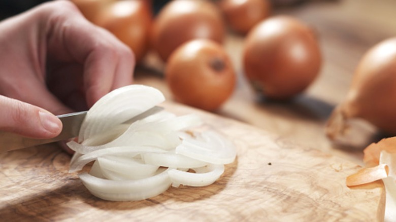 Person slicing onions on wood cutting board