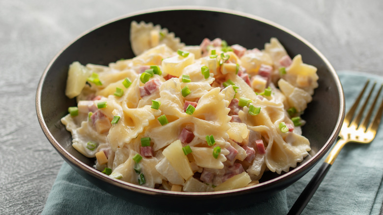 A bowl of bowtie pasta resting on a napkin on a stone surface next to a fork
