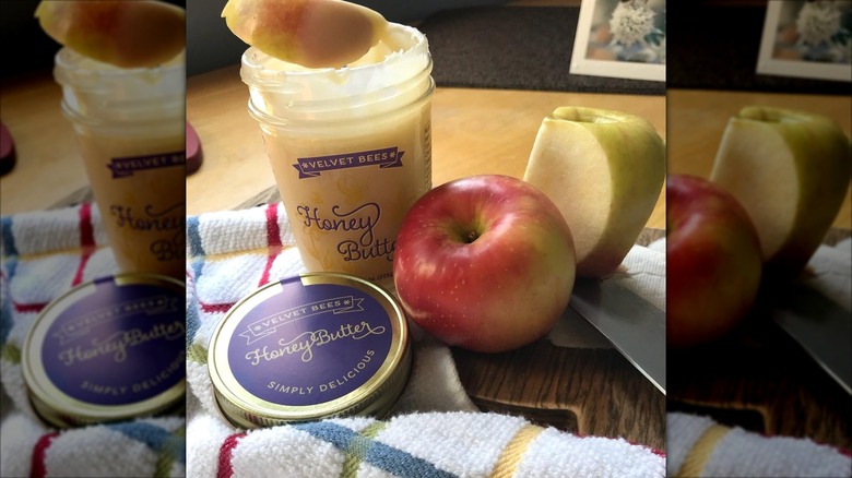 A jar of Velvet Bees Honey Butter next to apples, with a slice being dipped.