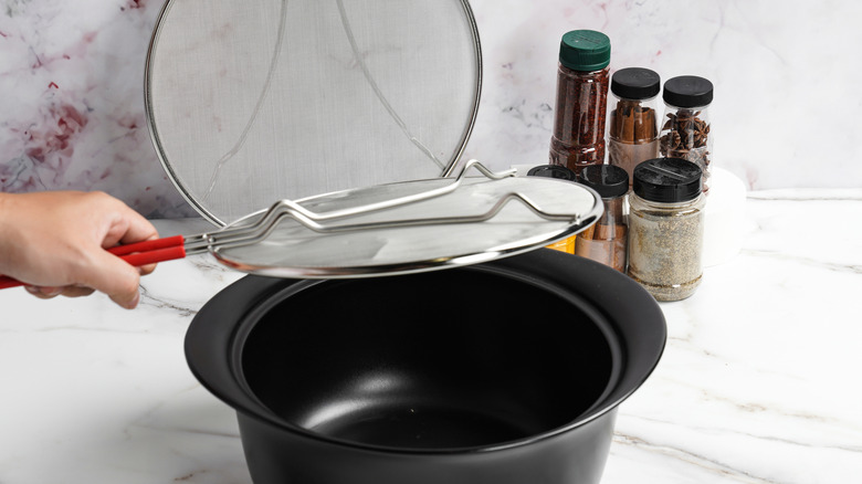 hand positioning splatter guard over pot