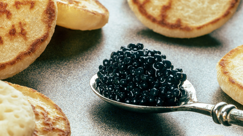 Silver spoonful of black caviar with blinis