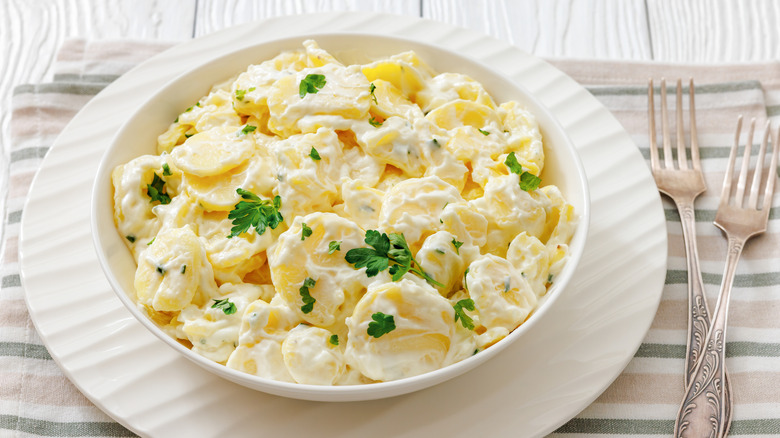 A bowl of potato salad sat on a neat place setting on a white wood style surface