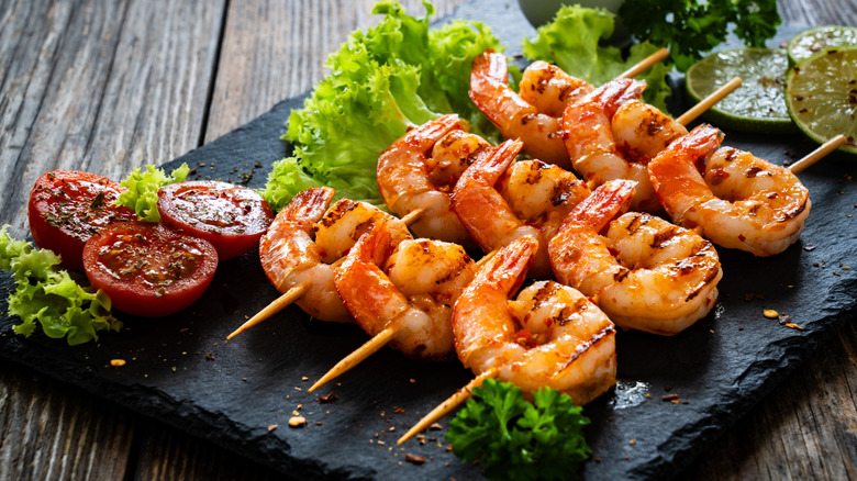 Grilled shrimp skewers served with tomatoes and lime.