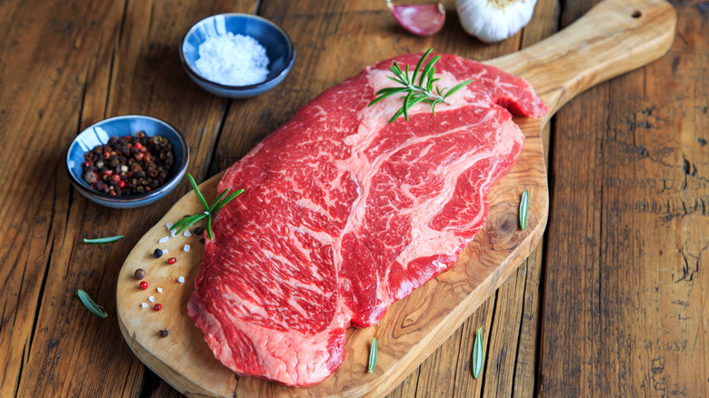 Raw chuck eye steak on wooden cutting board with seasonings