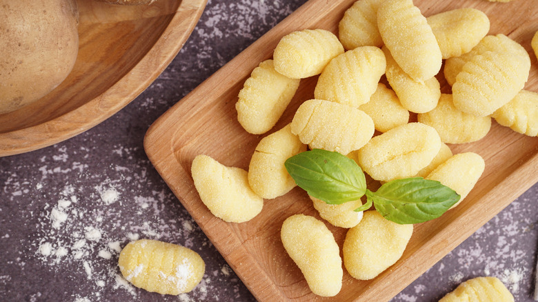 Raw gnocchi presented on a board with a basil leaf