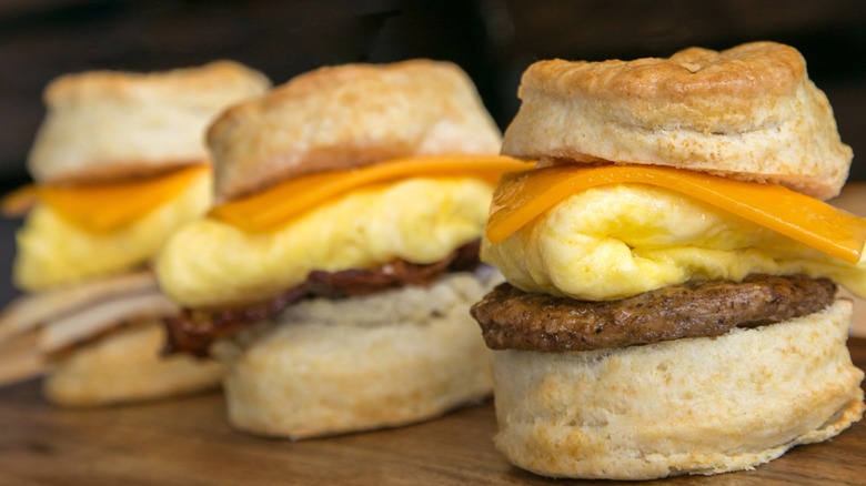 Three sausage, egg, and cheese biscuit sandwiches on a wooden board