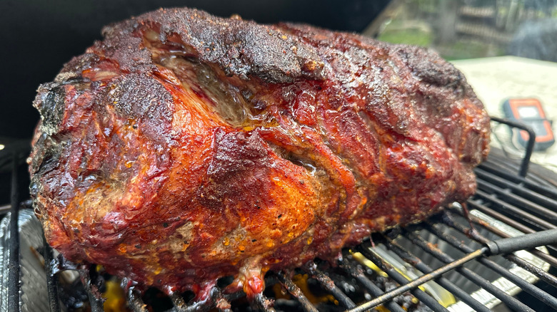 A juicy bone-in pork shoulder as it cooks in a smoker