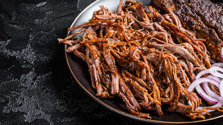 Pulled pork shoulder with red onions beside it on a black plate