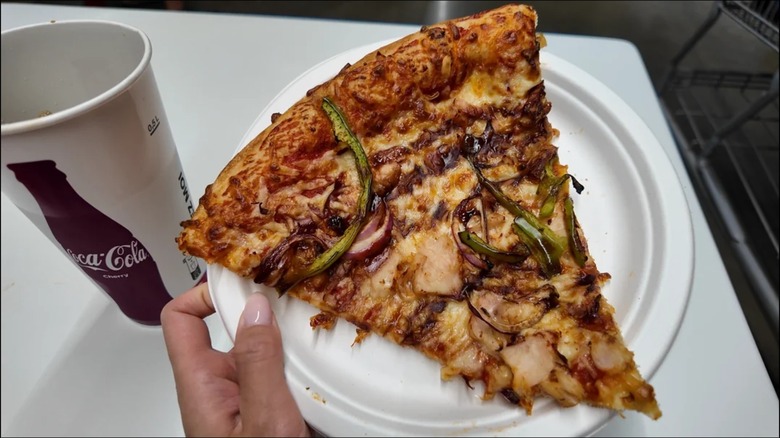 A person holding a plate with a slice of the BBQ Chicken Pizza from a Costco location in France.