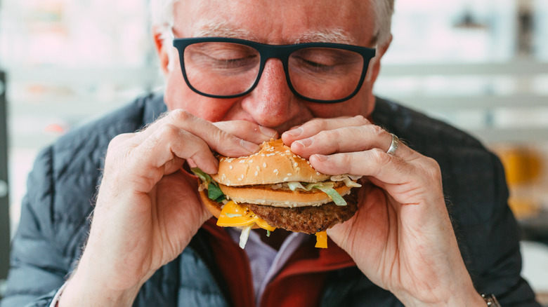 An elderly man taking a bite out of a cheeseburger.